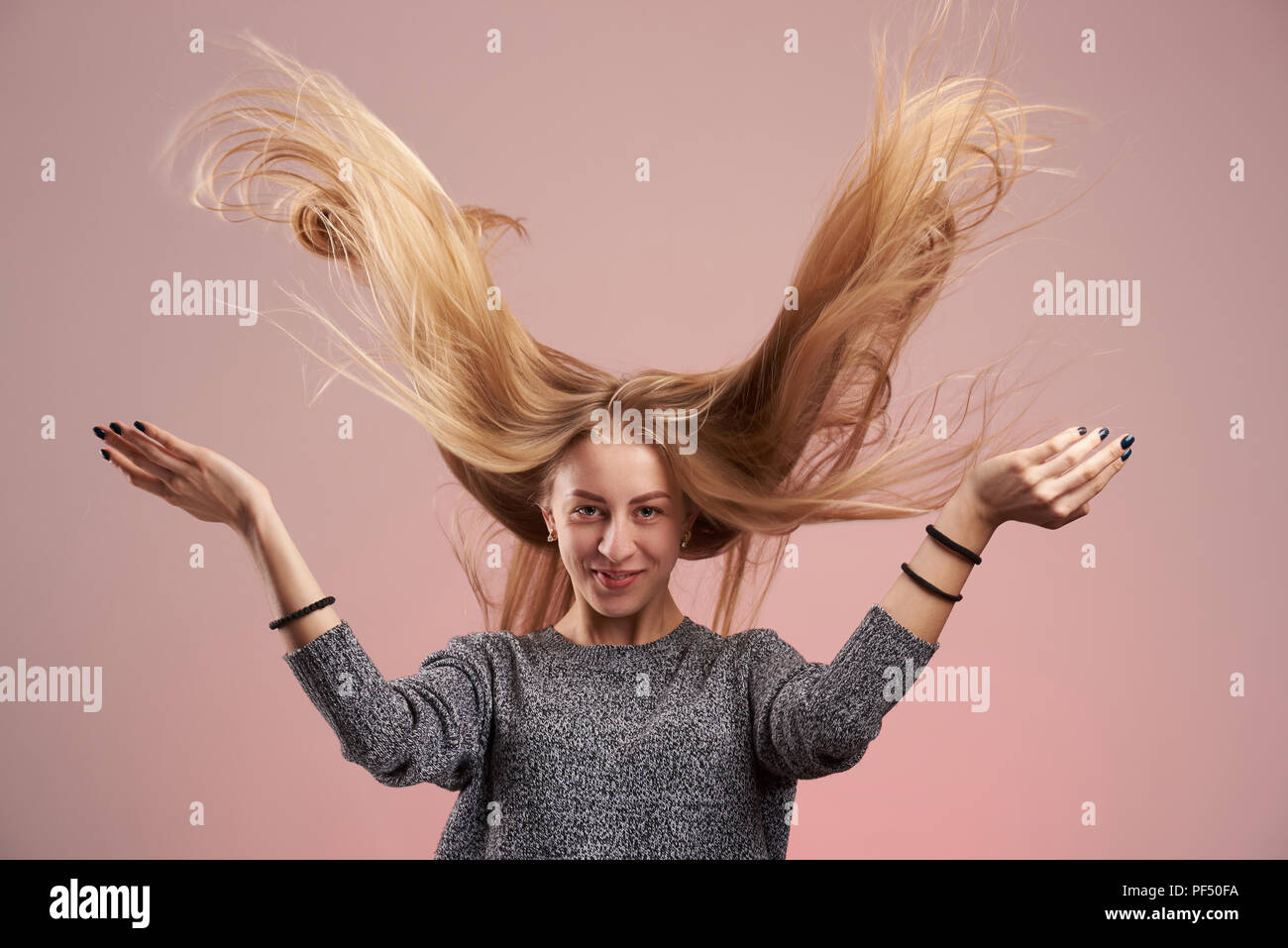 Frau mit fliegenden Haaren auf rosa Hintergrund. Lange blonde Haare Stockfoto