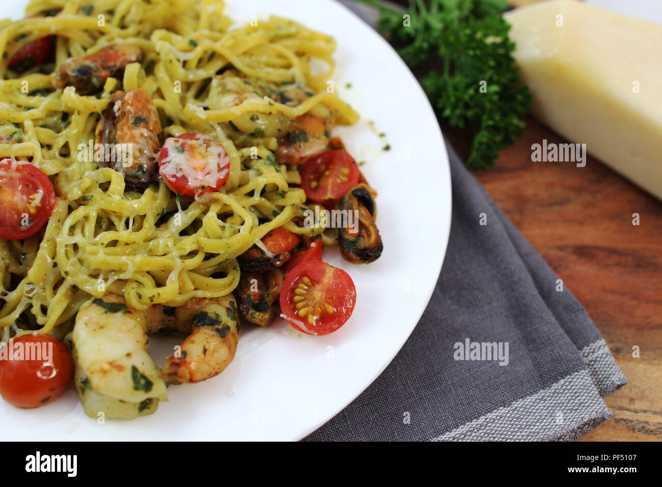 Pesto Linguine mit Tomaten, Garnelen und Muscheln auf einer weißen Platte. Stockfoto