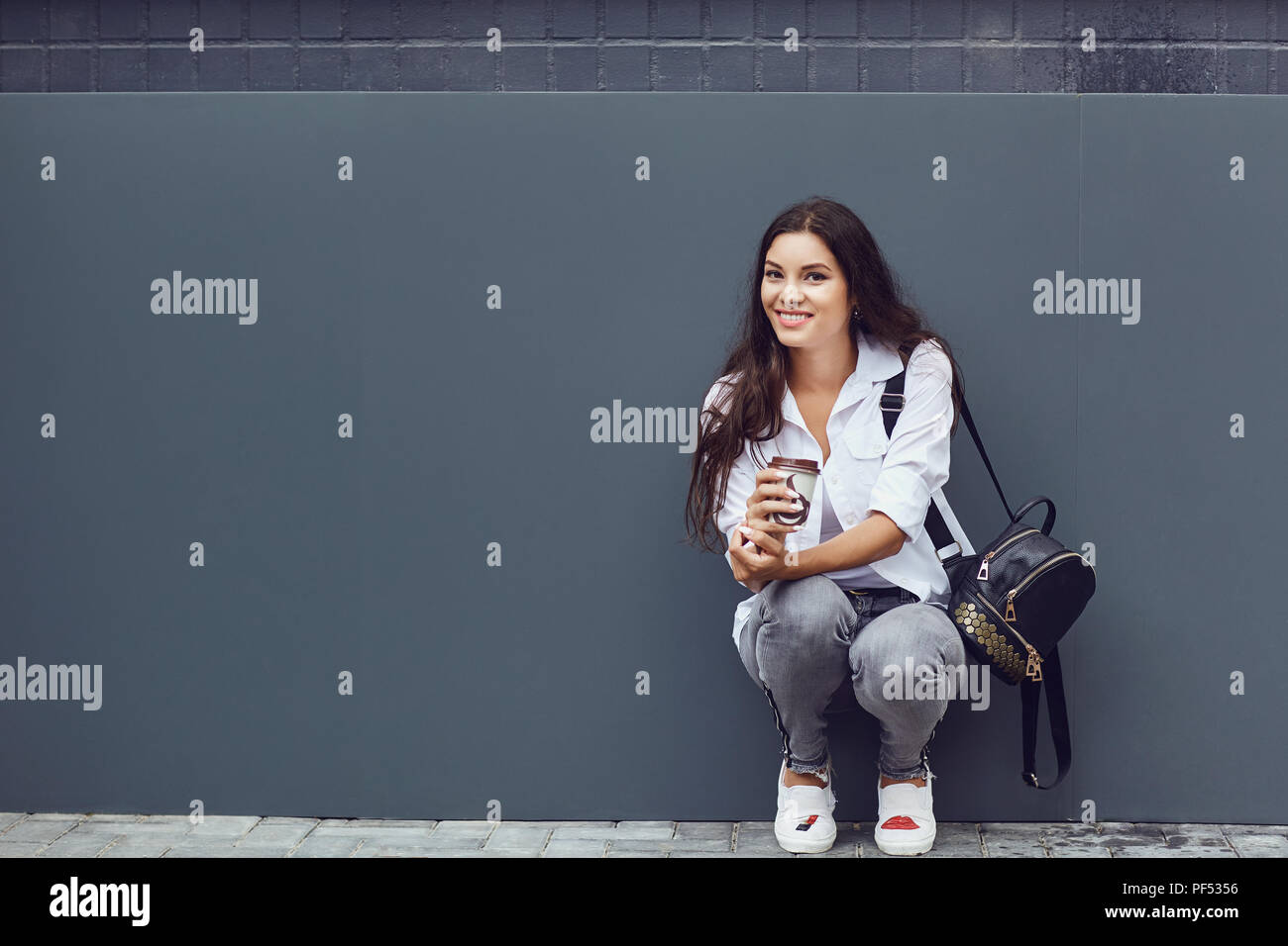 Eine brünette Mädchen mit einem Kaffeebecher lächelt Outdoor. Stockfoto