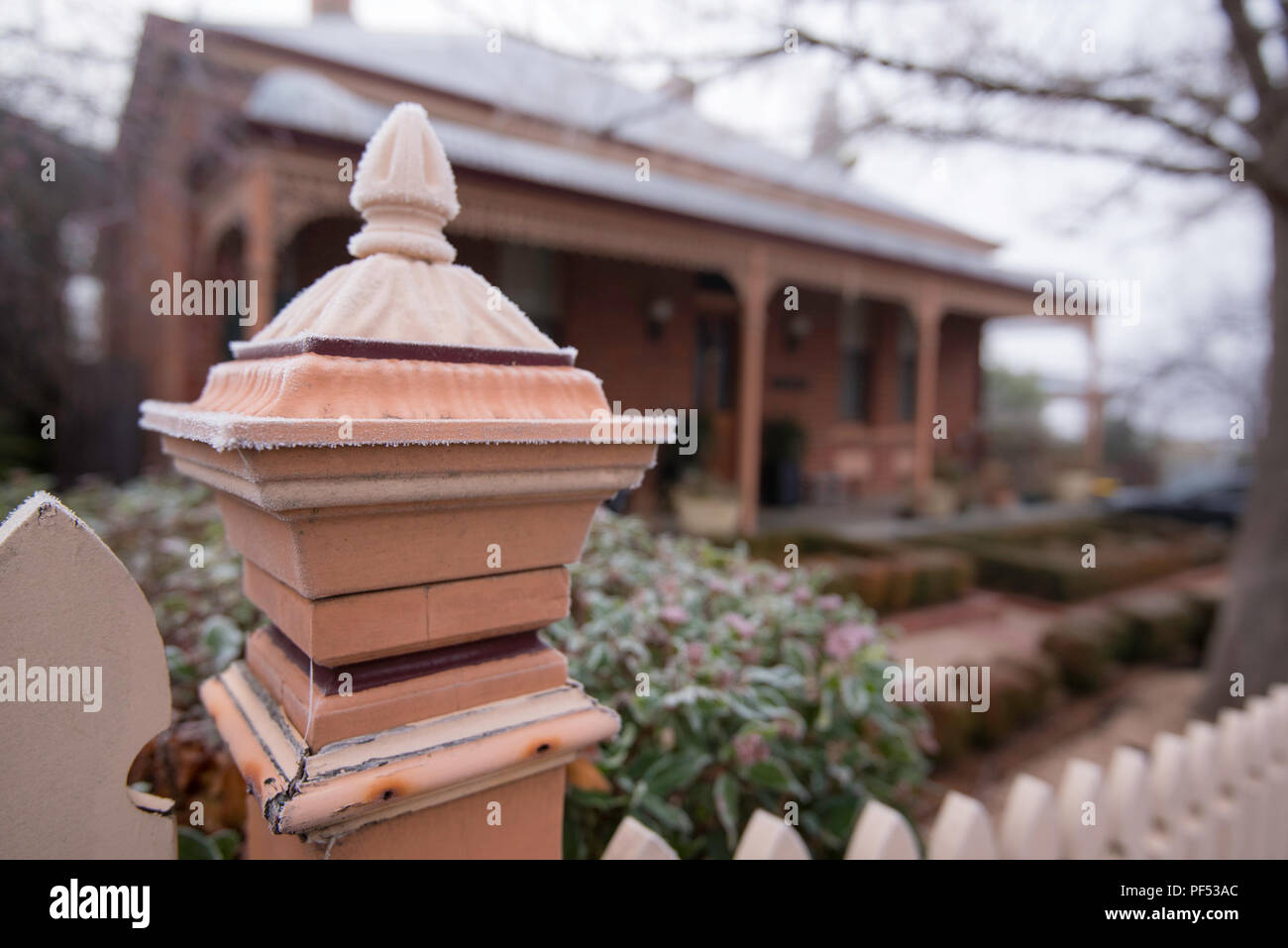 Ein sehr kalter Morgen, ein Holz Lattenzaun und Hedge im Vordergrund mit einer Föderation home mit Bull Nose Veranda und unscharf im Hintergrund Stockfoto