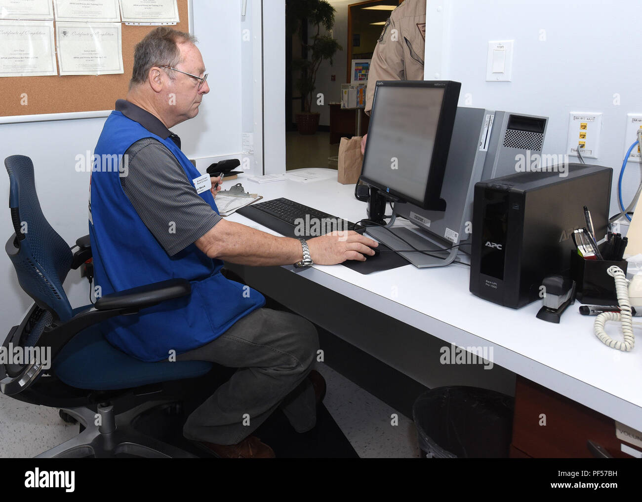 Naval Gesundheit Klinik Corpus Christi Rotes Kreuz Freiwillige, Pfr. Patrick Beck sucht Medikation des Patienten in die Nachfüll Apotheke im Medizinischen Heimathafen Lobby, Aug 13., 2018. Beck, von Corpus Christi, hat einem Diözesanpriester für 42 Jahre gewesen ist, ist ein pensionierter Luftwaffe Römisch-katholischen Kaplan, und hat sich freiwillig für 4 Jahre. Marine Foto von William Liebe Stockfoto