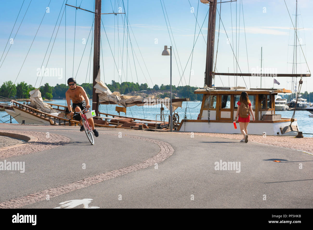 Helsinki Finnland Sommer, Blick auf einen Sommer morgen einen jungen Mann auf einem Fahrrad Radfahren auf einem Radweg entlang der Kaimauer im Hafen von Helsinki, Finnland. Stockfoto