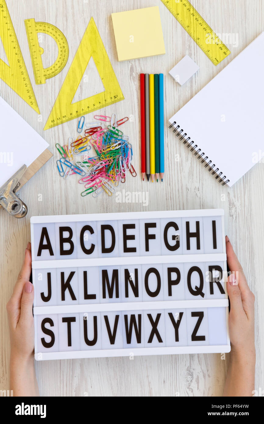 Zurück zum Konzept der Schule. Weibliche Hände halten moderne Brett mit Buchstaben von A bis Z Über weiß Holz- Hintergrund, Ansicht von oben. Zubehör für studieren. Stockfoto