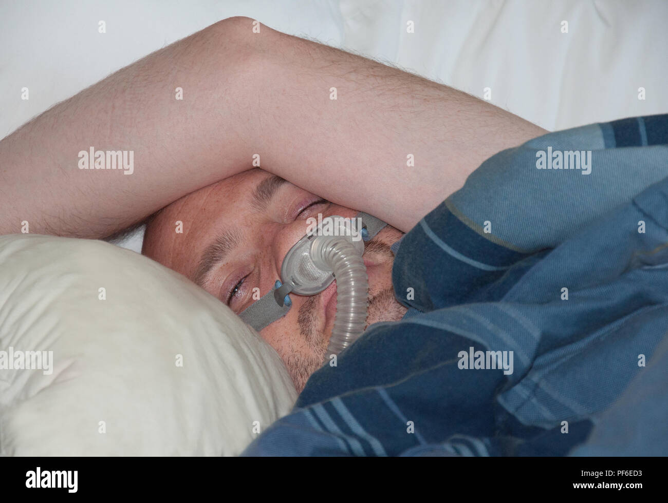 Dieser Kaukasischen mittleren Alter Mann trägt eine Nase CPAP-Maske, während im Bett lag. Die medizinische Behandlung zu Hause für Schlafapnoe. Stockfoto