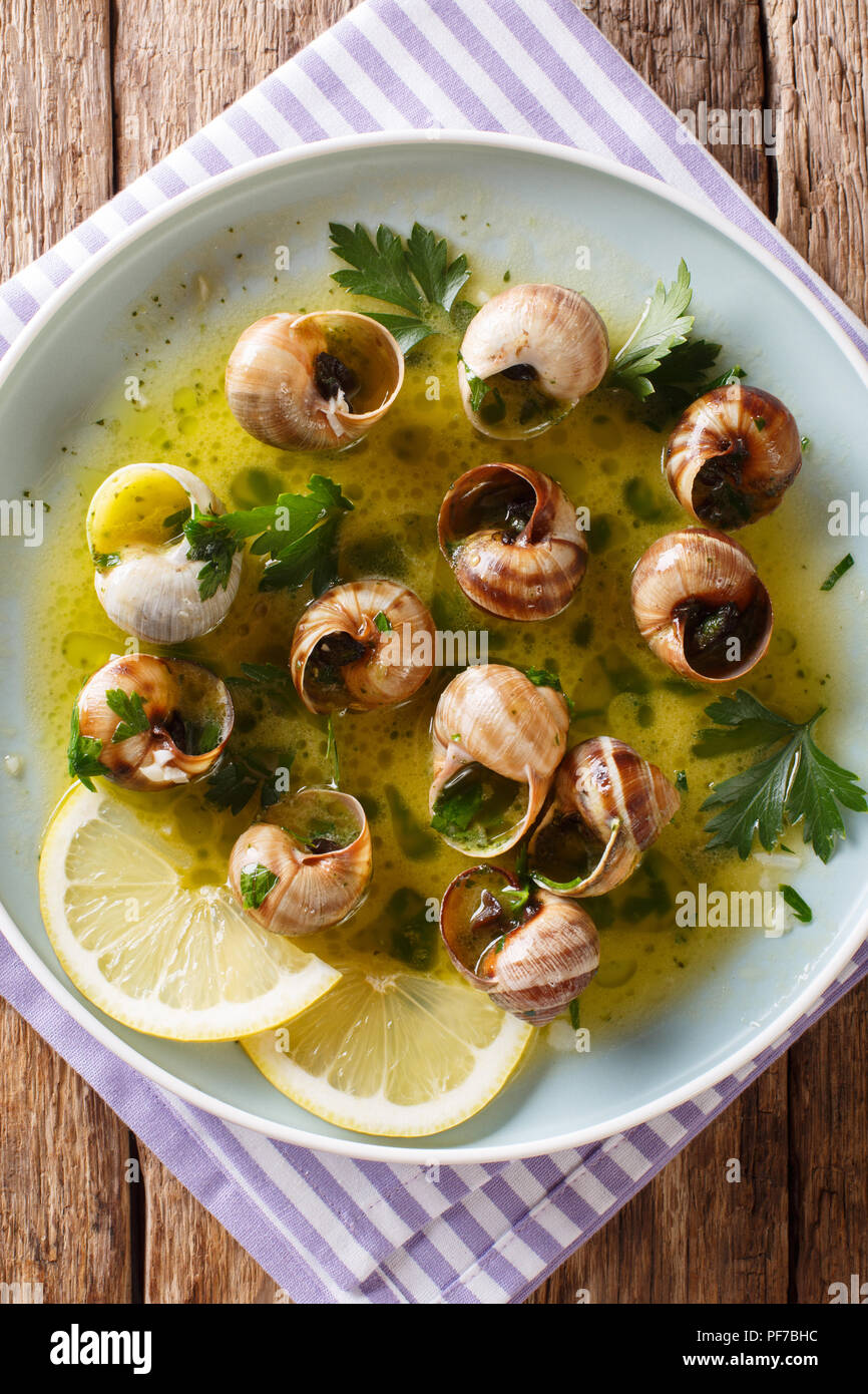 Würzige französische Schnecken, Escargot mit Butter, Petersilie, Zitrone und Knoblauch in der Nähe gekocht - bis auf einen Teller auf dem Tisch. Vertikal oben Ansicht von oben Stockfoto