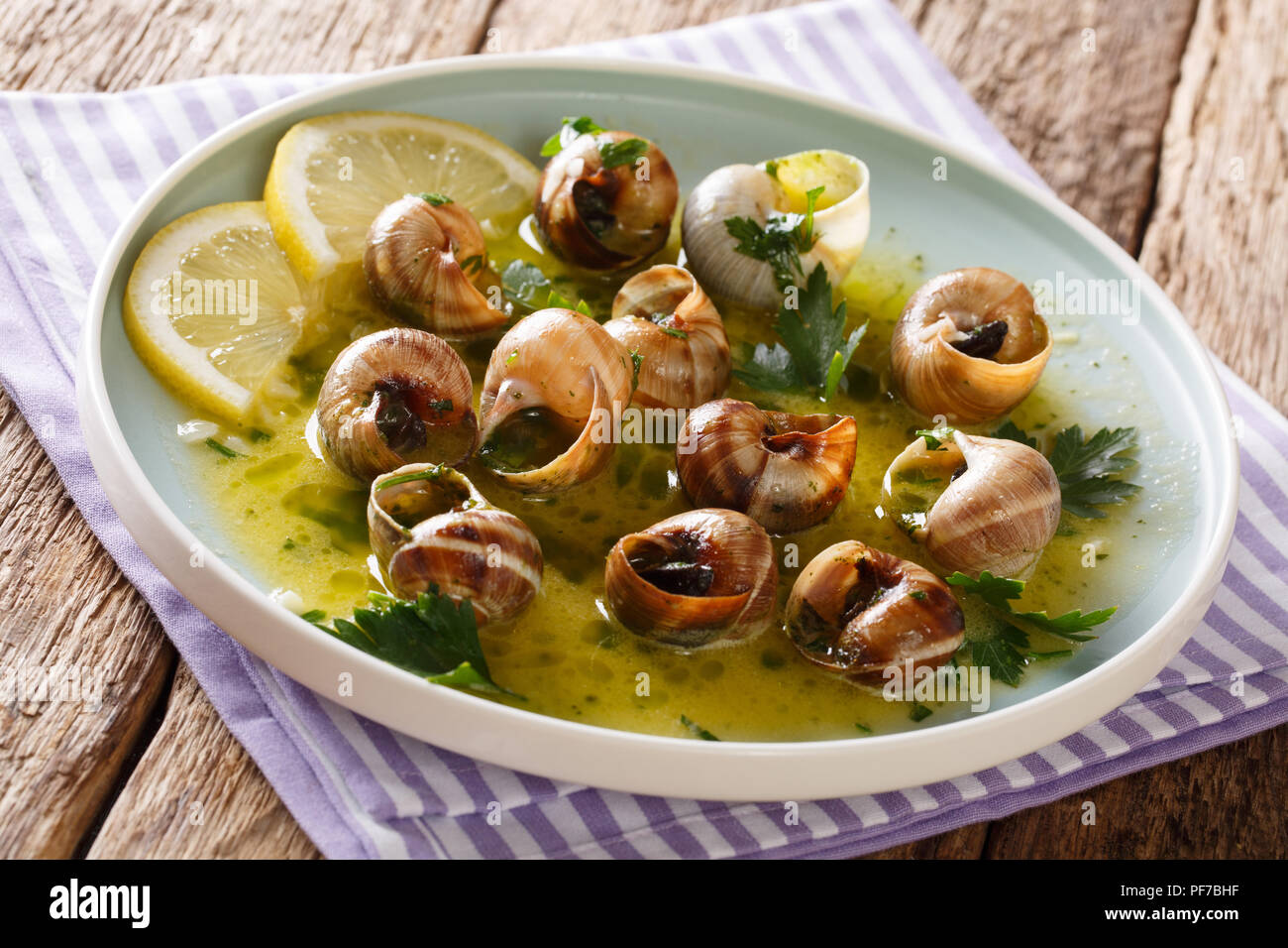 Würzige französische Schnecken, Escargot mit Butter, Petersilie, Zitrone und Knoblauch in der Nähe gekocht - bis auf einen Teller auf dem Tisch. Horizontale Stockfoto