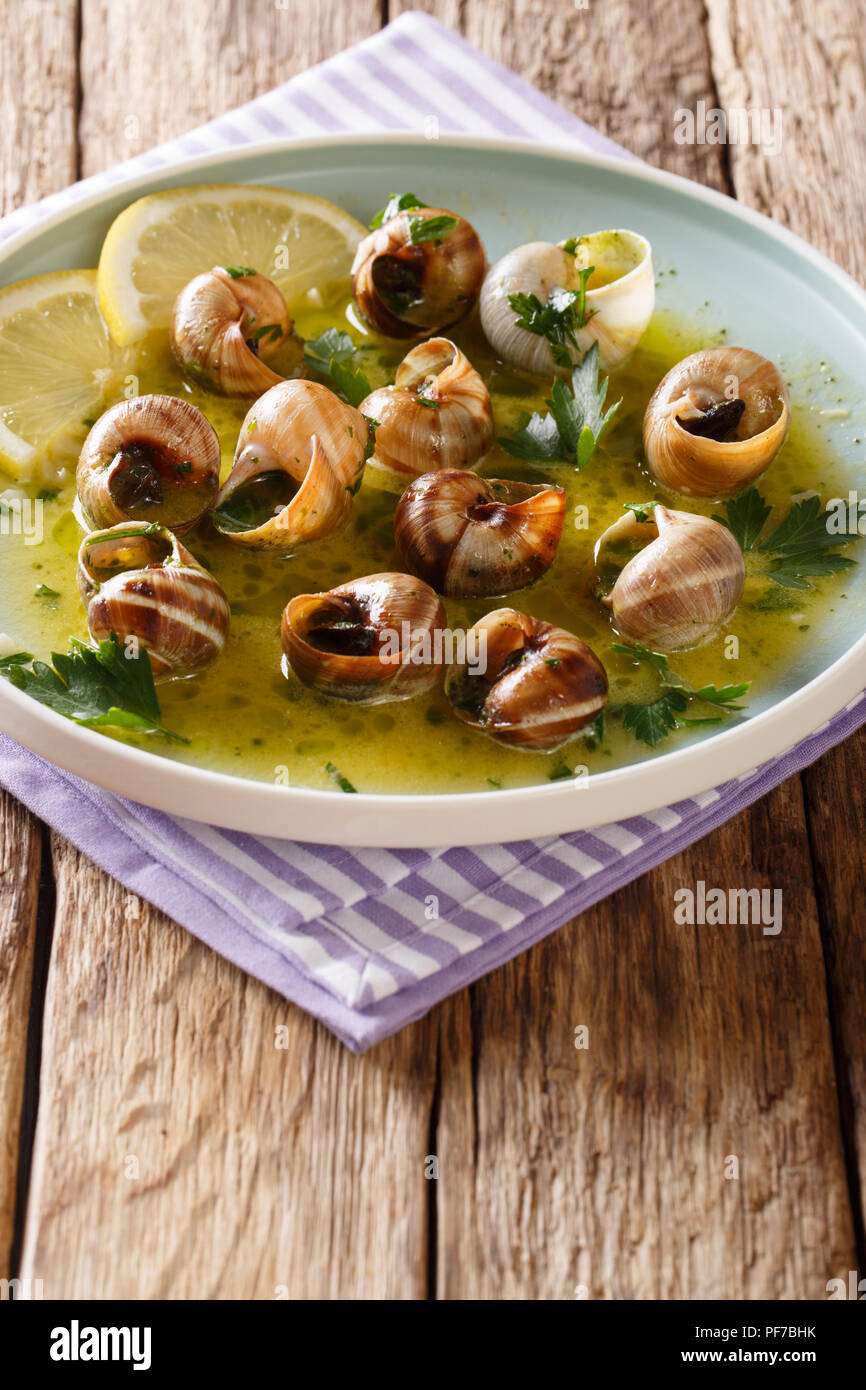 Französische Küche: Escargot mit Butter, Kräutern und Knoblauch close-up auf einem Teller auf dem Tisch. Vertikale Stockfoto