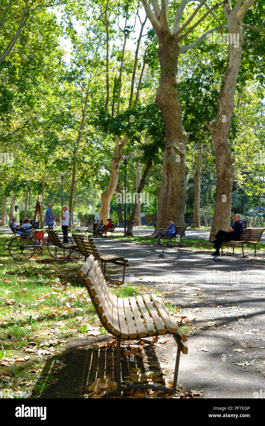 Menschen genießen und entspannen an einem Sonntagmorgen in der Sonne im Park mit Bänken gesäumt. Piacenza, Italien, Europa. Stockfoto