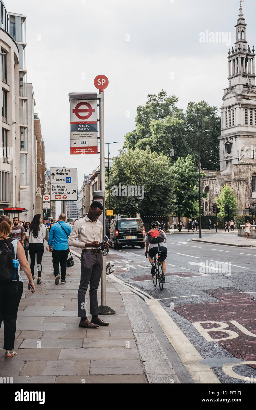 Mann sein Handy surfen beim Warten auf einen Bus auf dem Bus die St. Paul's Stop in der Stadt London, berühmten Londoner Financial District. Stockfoto