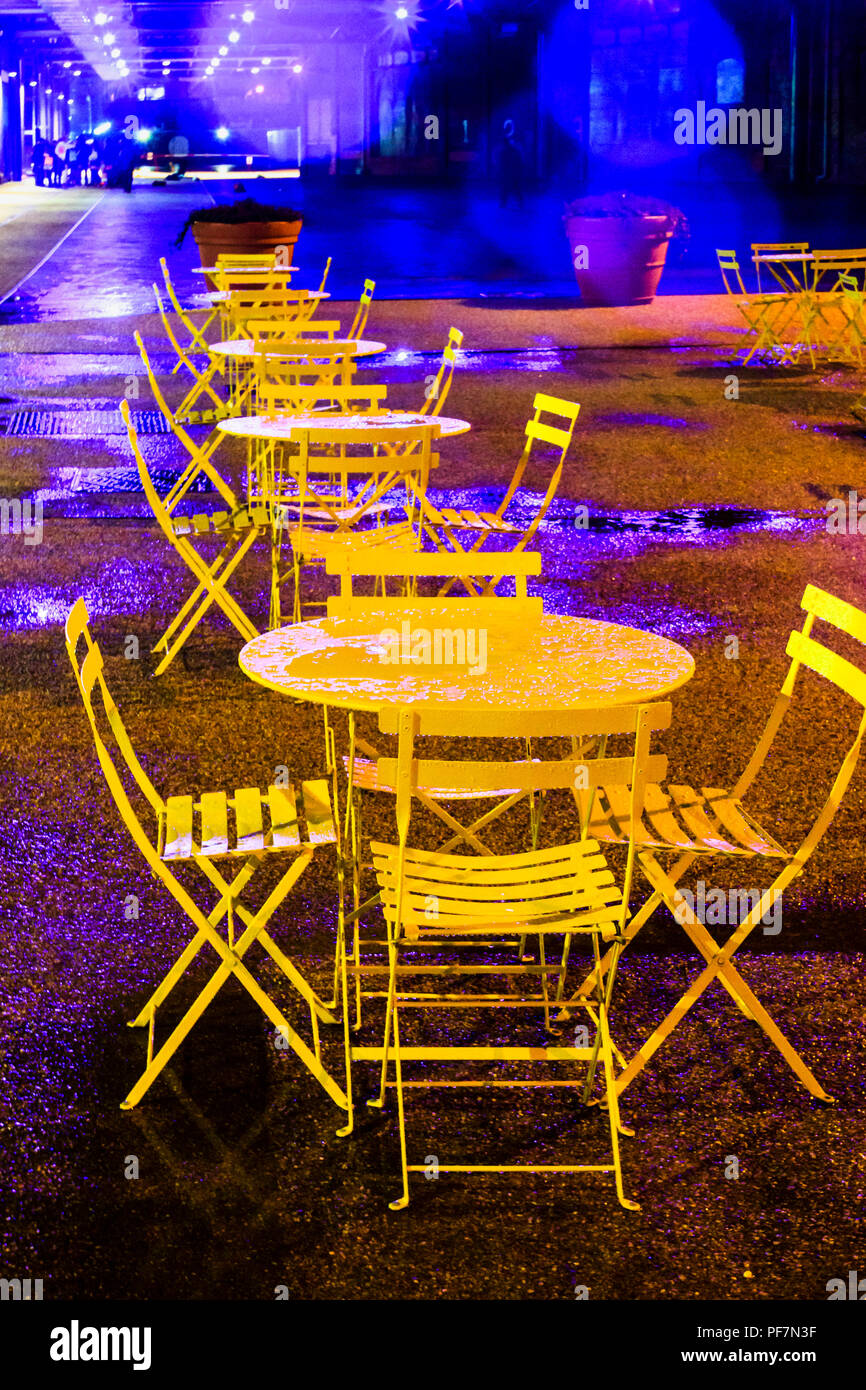 Nicht belegte Gelb - Metall Tische und Stühle in der Regen in der Nacht gemalt, King's Cross, London, UK, 2012 Stockfoto