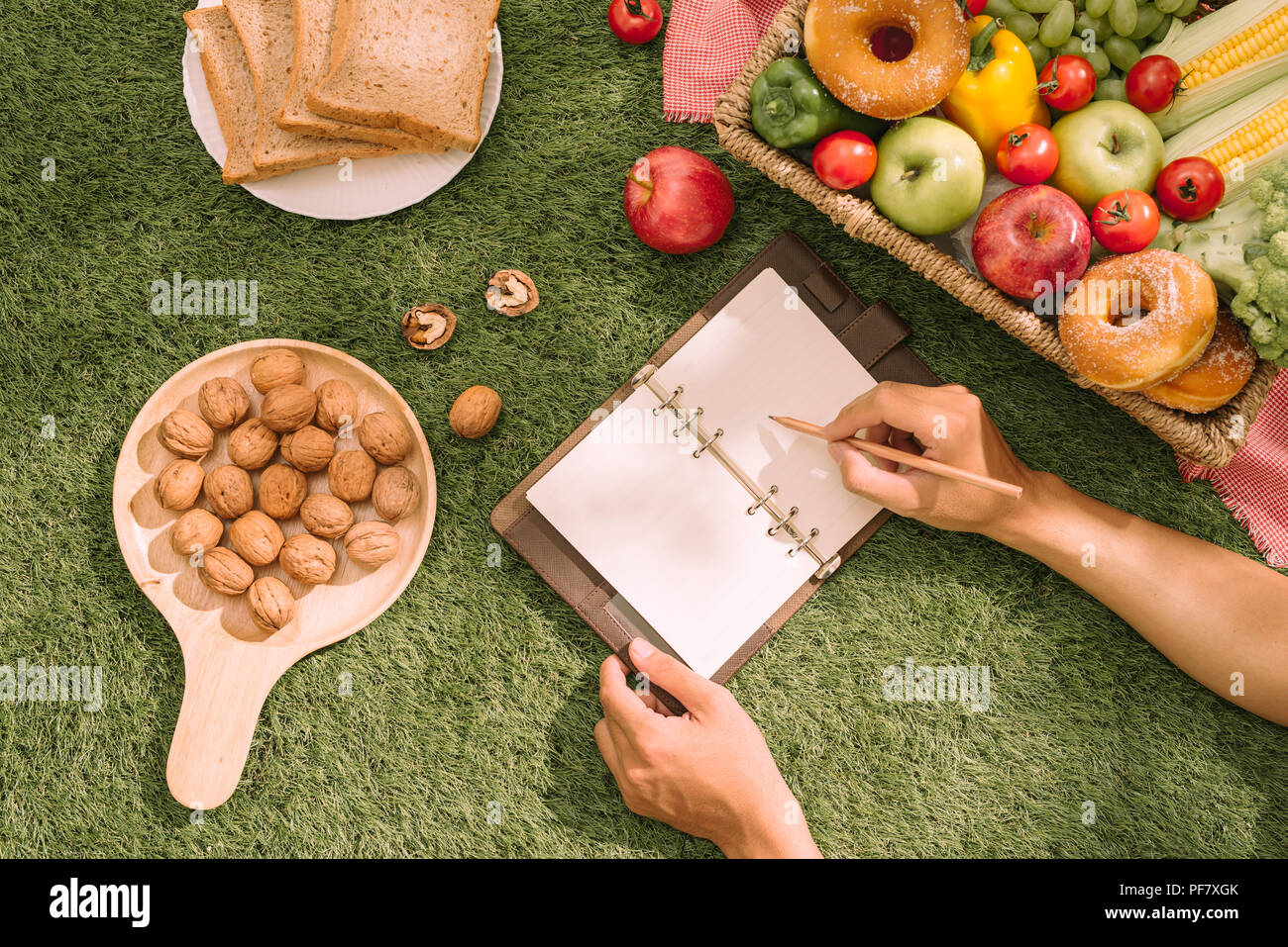 Picknick Weidenkorb mit Essen, Brot, Obst und Orangensaft auf einer rot-weiß karierten Tuch in das Feld mit der grünen Natur Hintergrund. Picknick conce Stockfoto