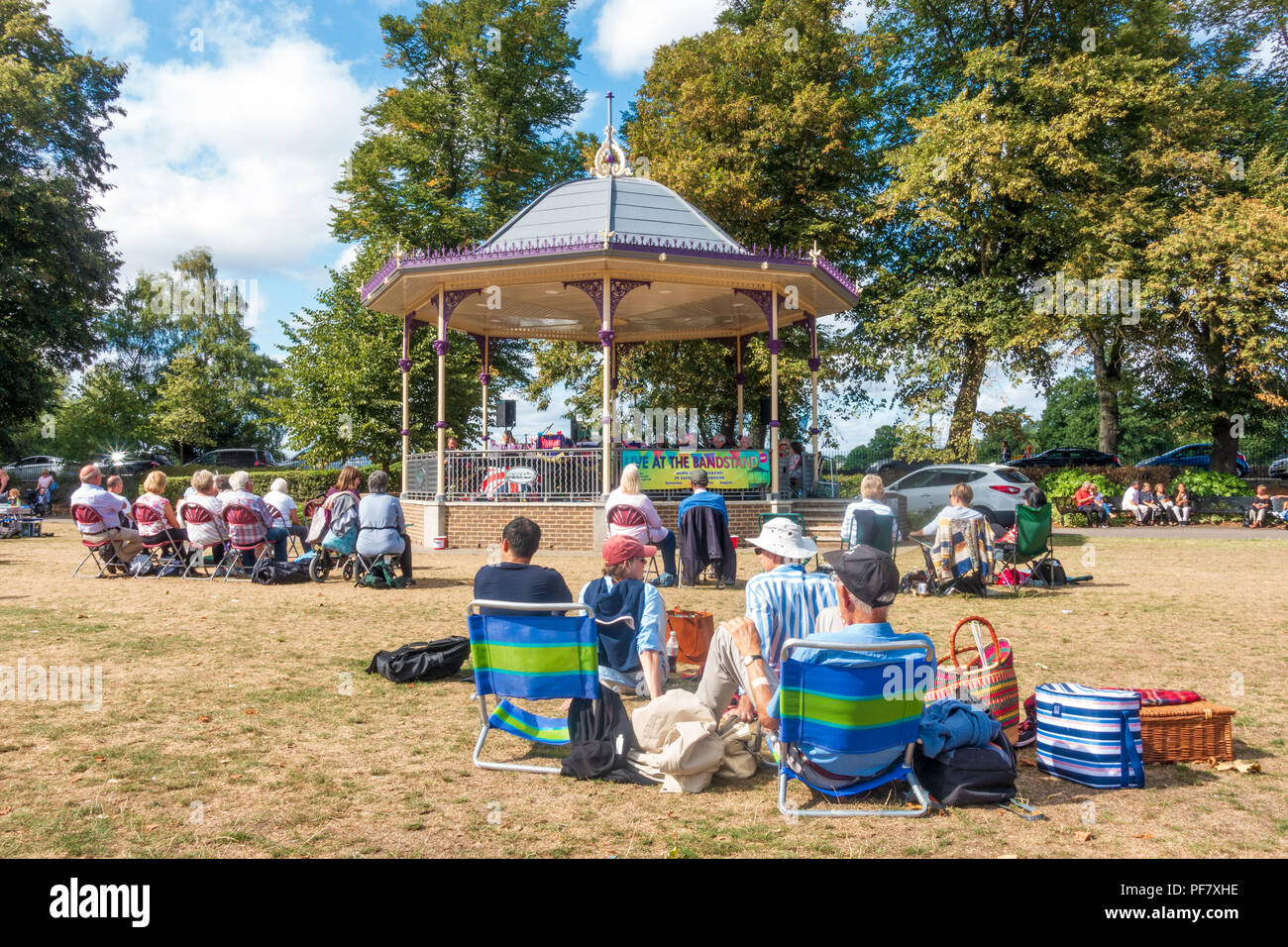 Eine Band spielt ein kostenloses Konzert in der Band stand in Alexandra Gärten in Windsor, UK. Die Leute sitzen auf Klappstühlen, benchses und der Boden zu beobachten. Stockfoto