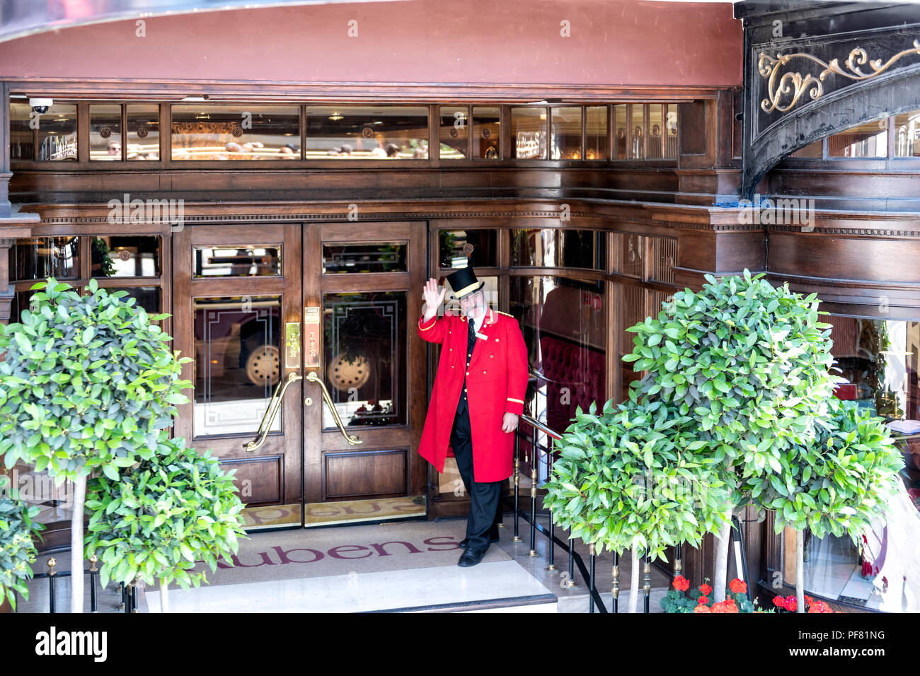 London, Großbritannien, 22. Juni 2018: Porter, Pförtner in traditioneller Kleidung, Kleidung, Hut, roten Kleid, Mantel an Rubens Hotel, inn Eingang Hand winken Stockfoto