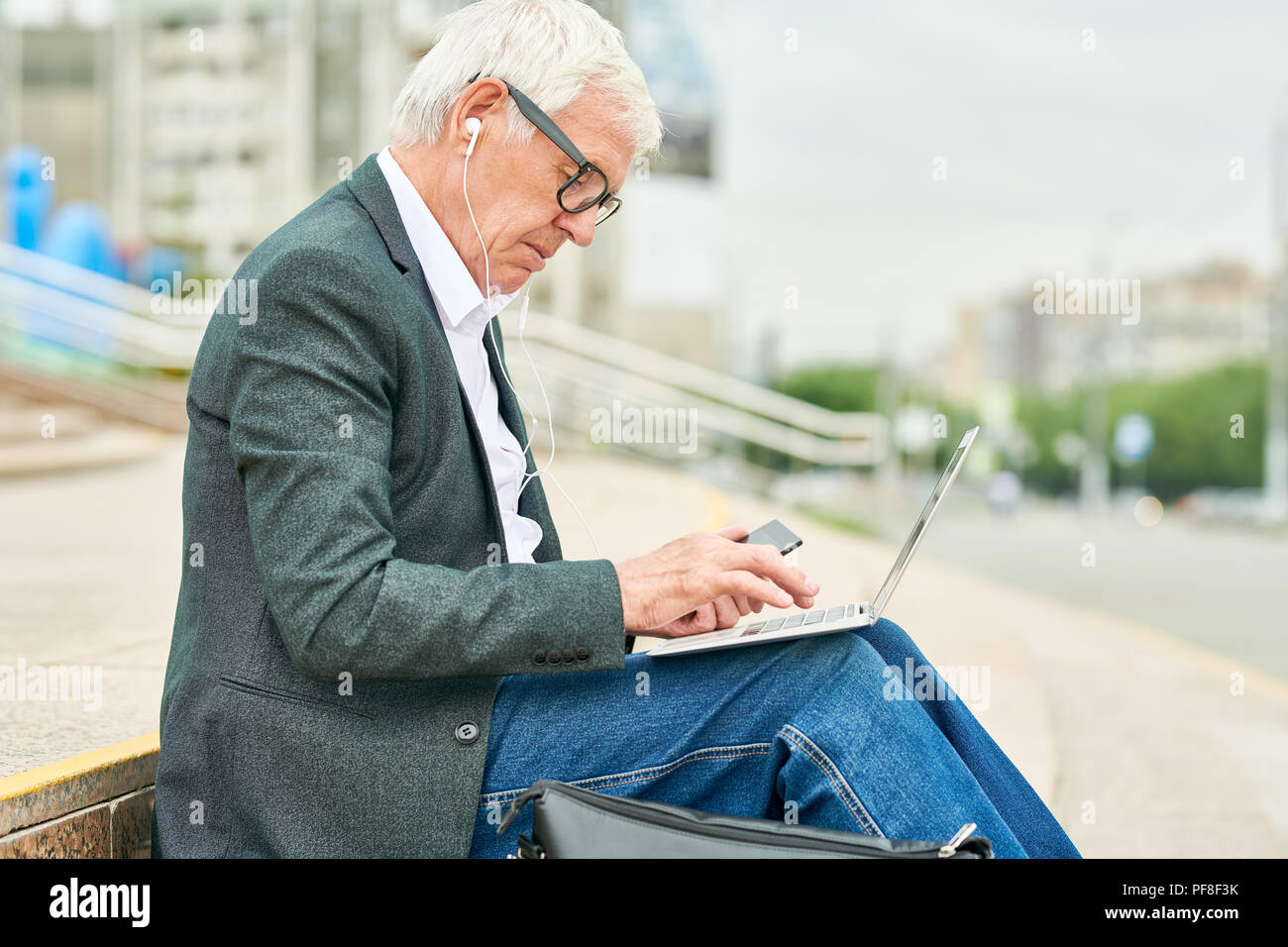 Alter Geschäftsmann mit Laptop und Anhören von Musik Stockfoto