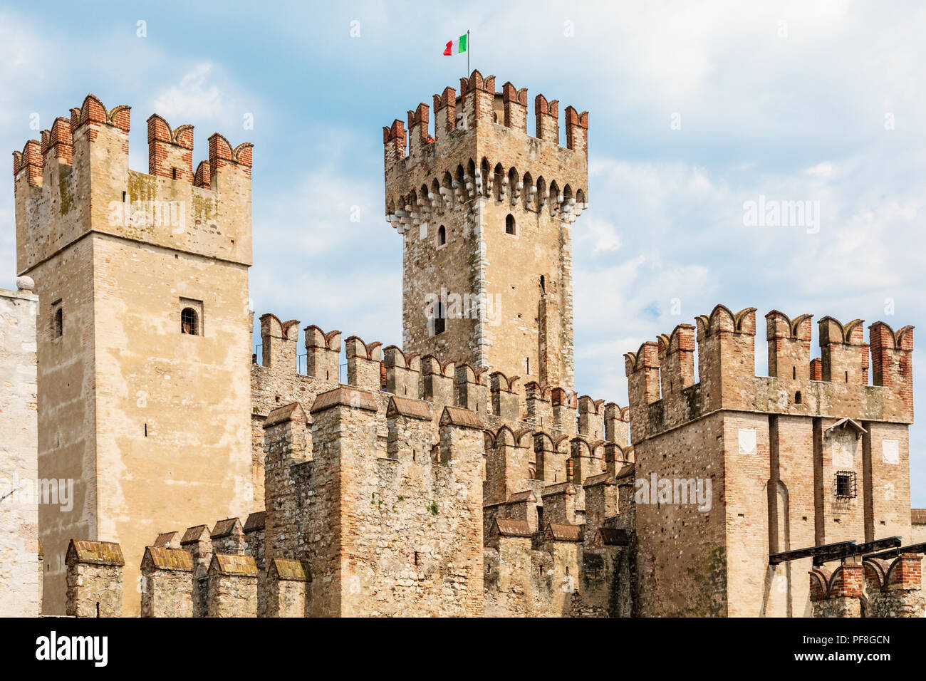 Die Wälle der mittelalterlichen Burg Sirmione am Gardasee in der Region Lombardei in Italien. Die Burg ist gegen einen blauen Himmel mit einem italienischen Flagge Stockfoto