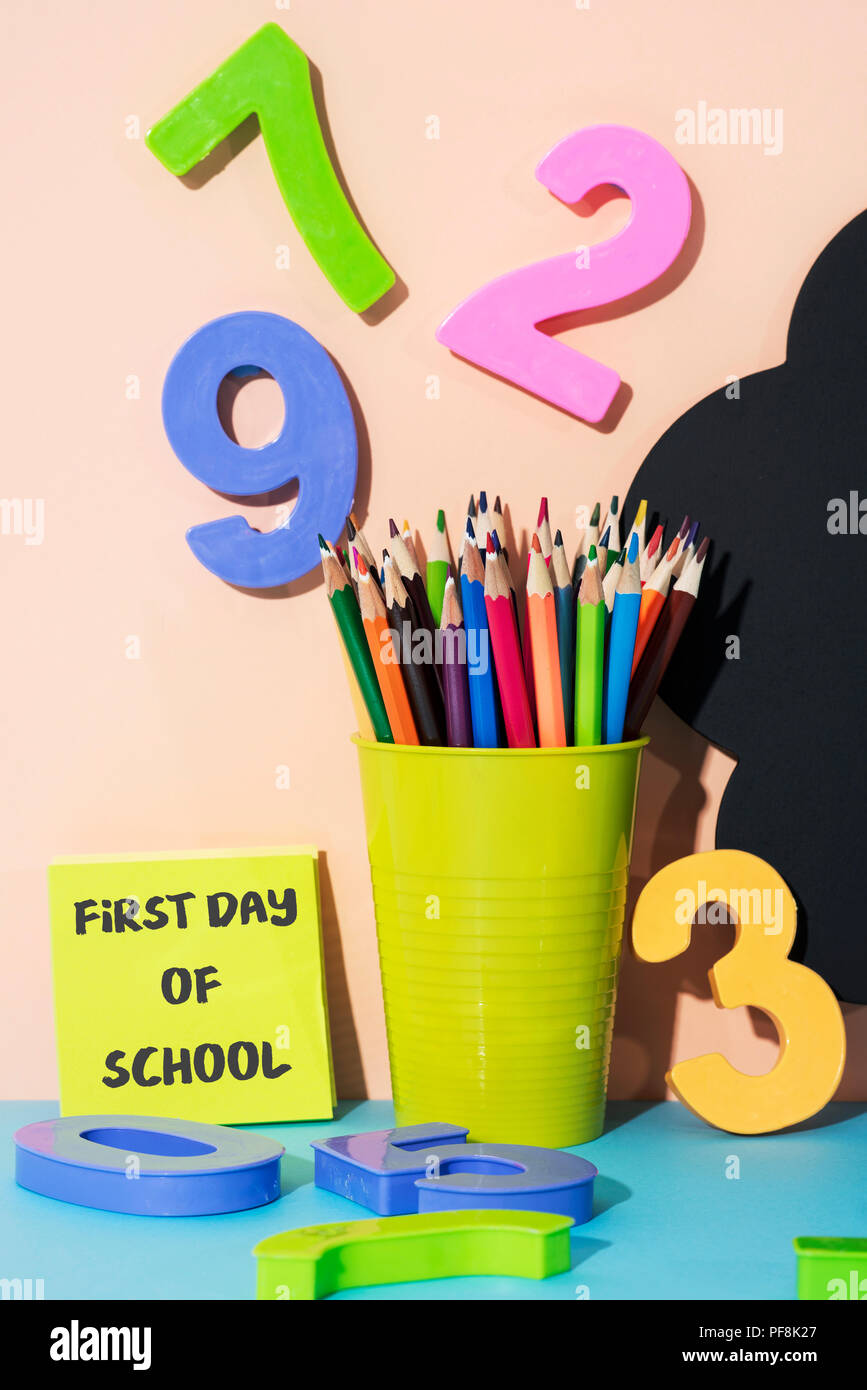 Topf mit einem Bleistift bleistift Farbstifte in verschiedenen Farben, einige drei-dimensionale Zahlen in verschiedenen Farben und den Text der erste Schultag geschrieben in Einem Stockfoto