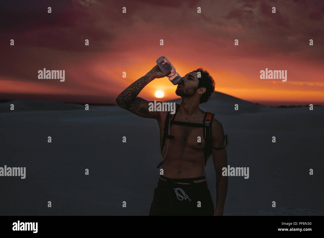 Athlet Trinkwasser bei Sonnenuntergang in der Wüste. Mann, die Pause nach dem Training in der Wüste. Stockfoto