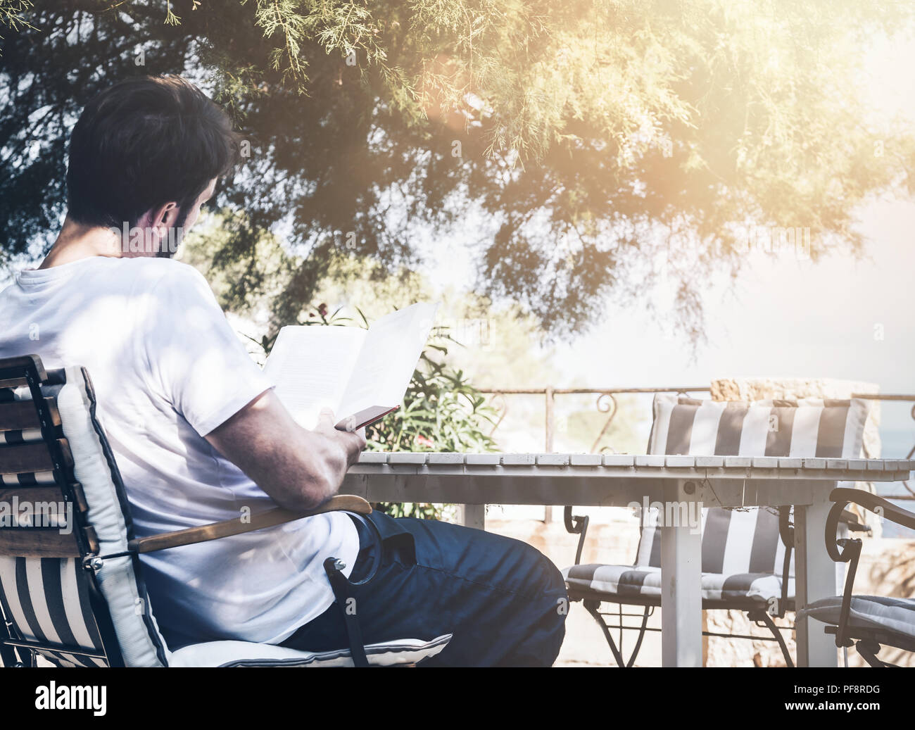 Mann sitzt im Garten Tisch ein Buch lesen Stockfoto