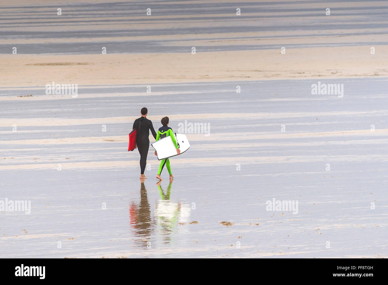 Vater und Sohn Anzüge tragen und Durchführung body Boards zu Fuß auf den Fistral Beach in Cornwall. Stockfoto