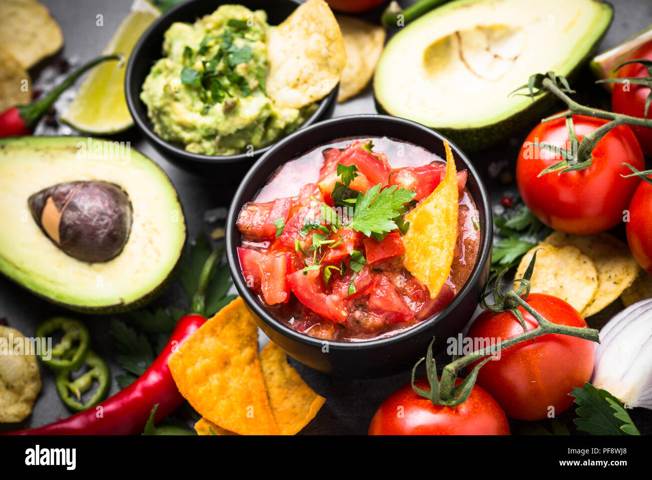 Lateinamerikanische mexikanisches Essen party Soße Guacamole, Salsa, Chips und Zutaten auf Schwarz. Stockfoto