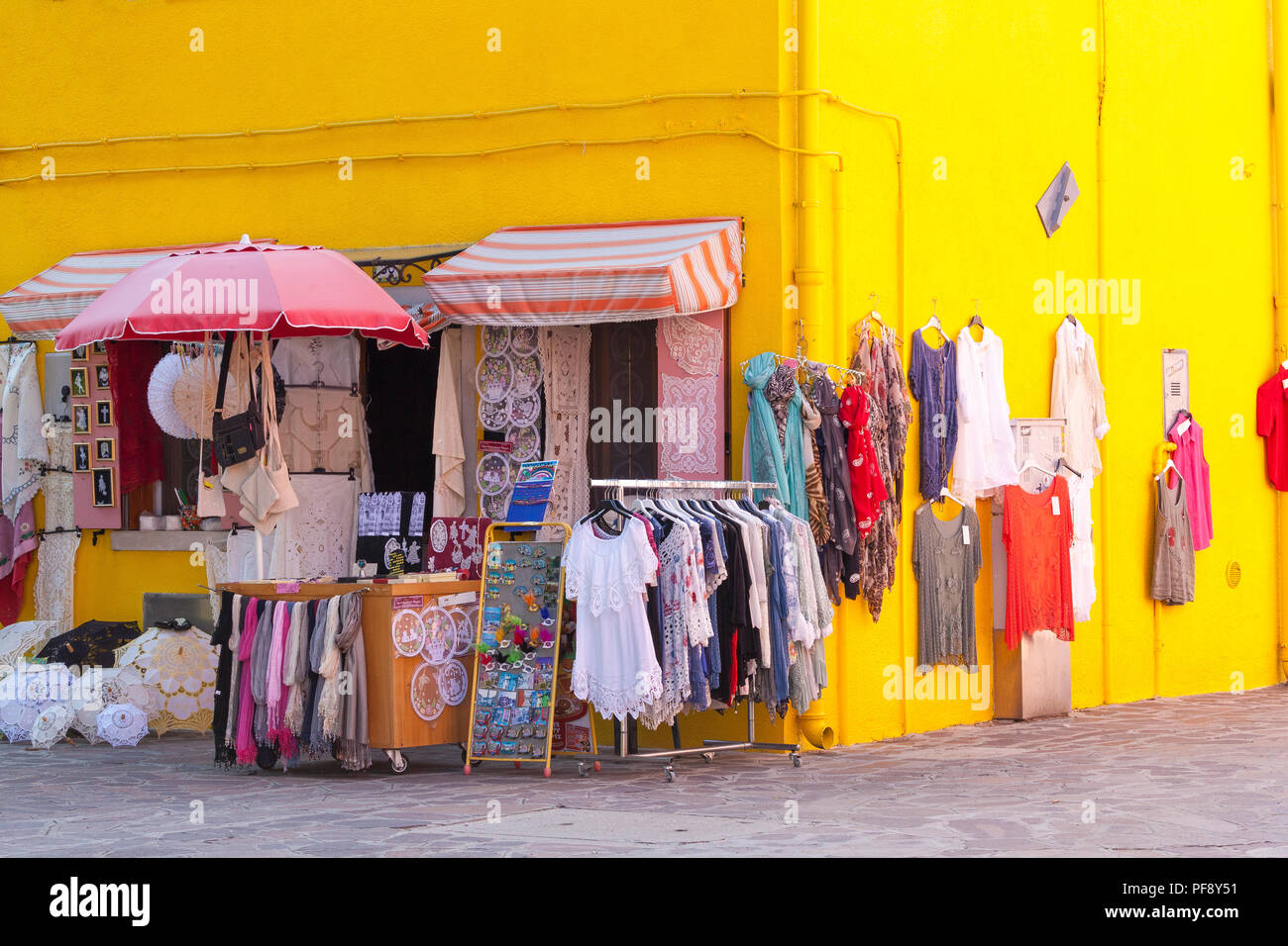 Sonnenuntergang in der farbenfrohen Fischerdorf auf der Insel Burano, Venedig, Venetien, Italien. Leuchtend gelb Shop mit Anzeige von Kleidung, Burano Spitze und Souvenirs Stockfoto