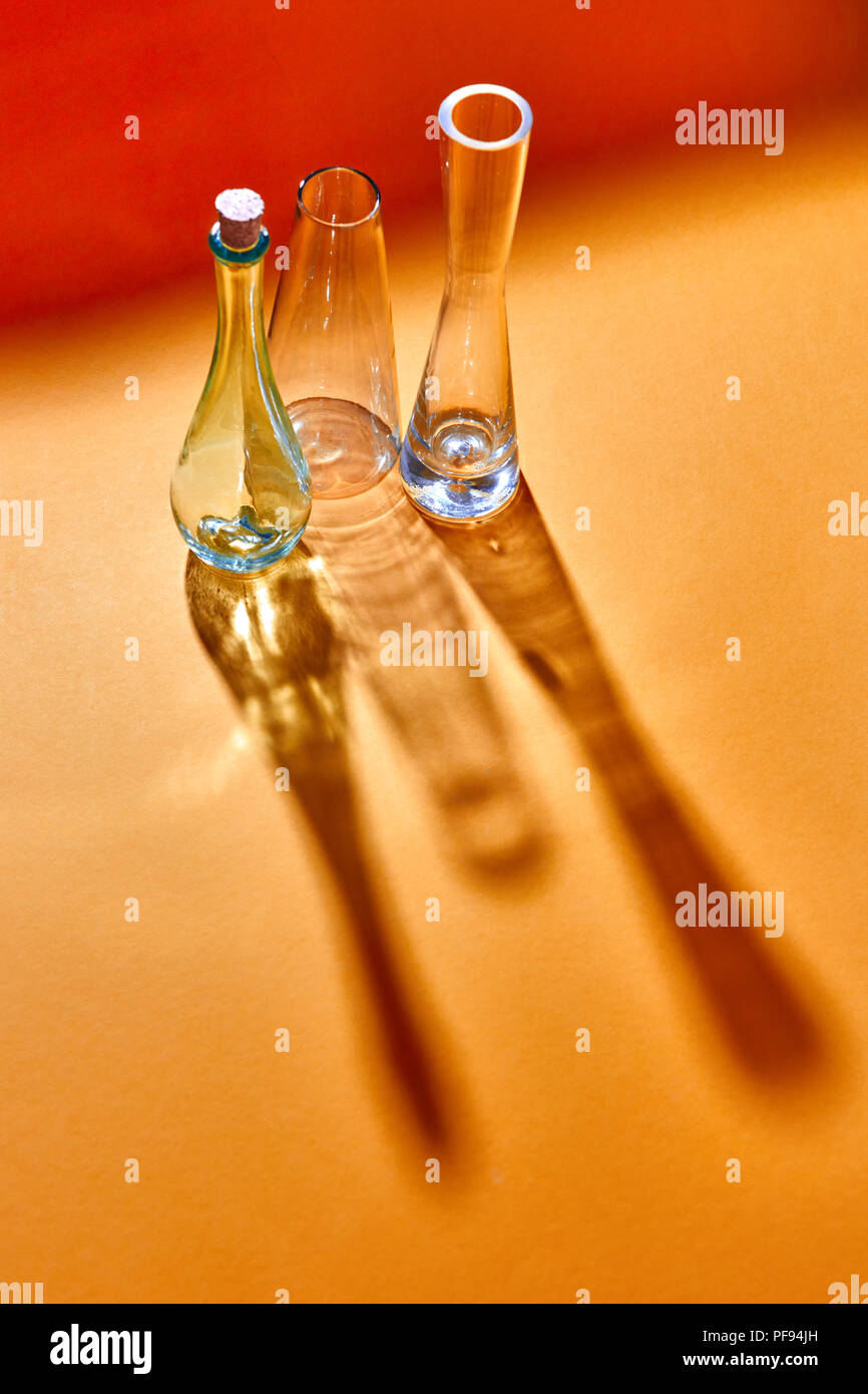 Leere Glas Vasen mit langen Schatten auf einem doutone rot gelb Papier Hintergrund. Stockfoto