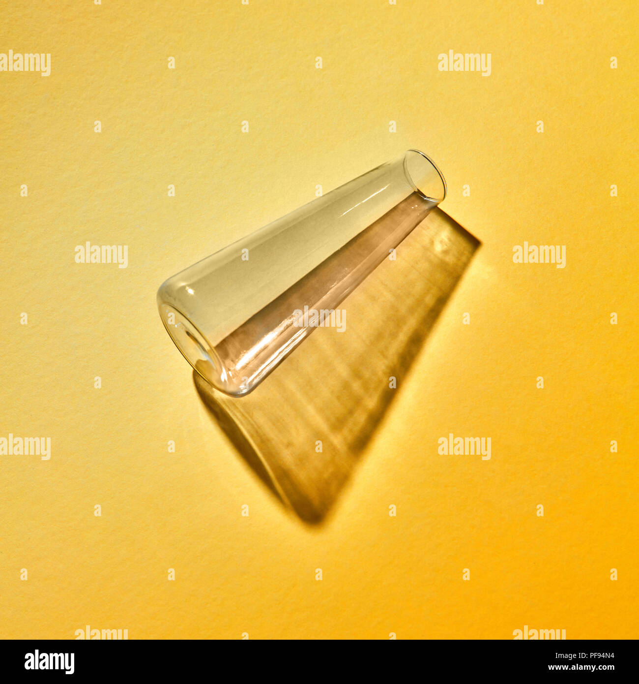 Ein transparentes Glas Vase leer liegt auf gelbem Papier Hintergrund mit weichen Schatten Stockfoto