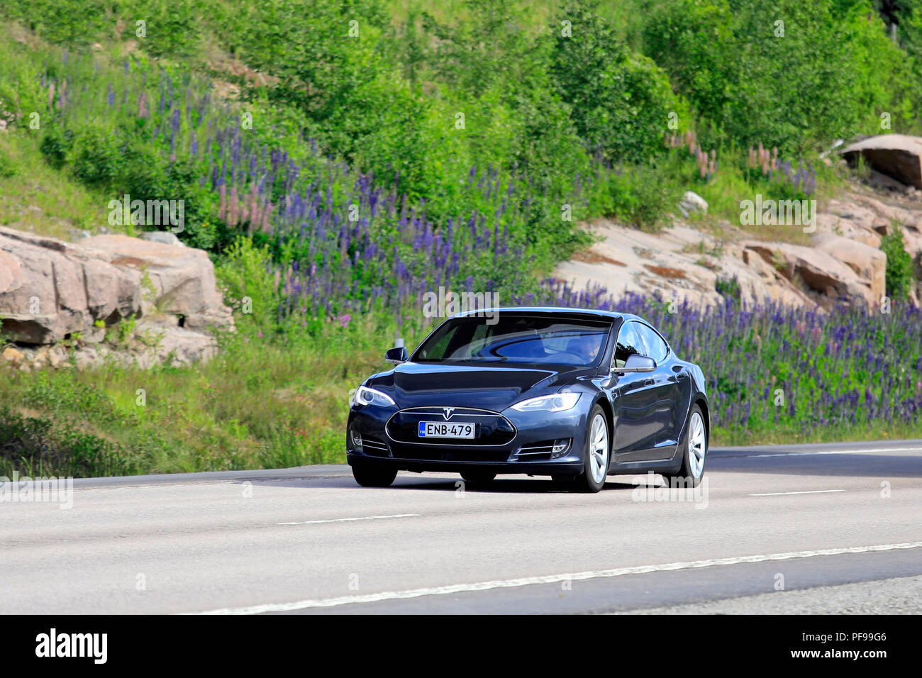 Vaajakoski, Finnland - 16. Juni 2018: Schwarz Tesla Model S elektrische Auto fährt entlang der Autobahn im Sommer, grüne Sträucher und Blumen in den Hintergrund. Stockfoto