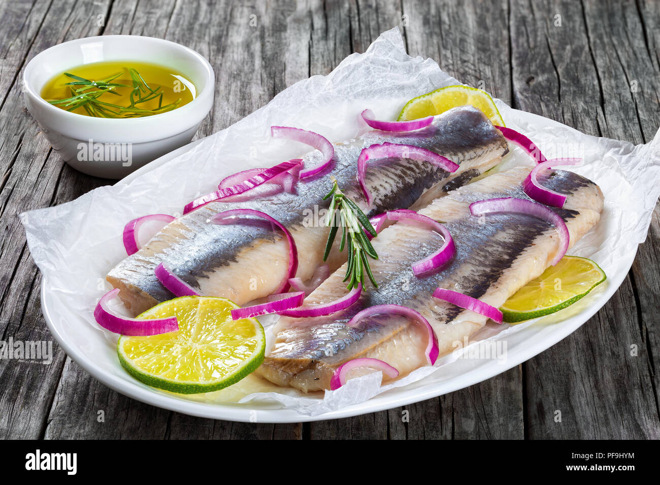 Heringsfilets mit Zwiebel und Kalk Schichten auf Pergamentpapier auf einem ovalen Teller auf einem alten rustikalen Tisch, close-up Stockfoto