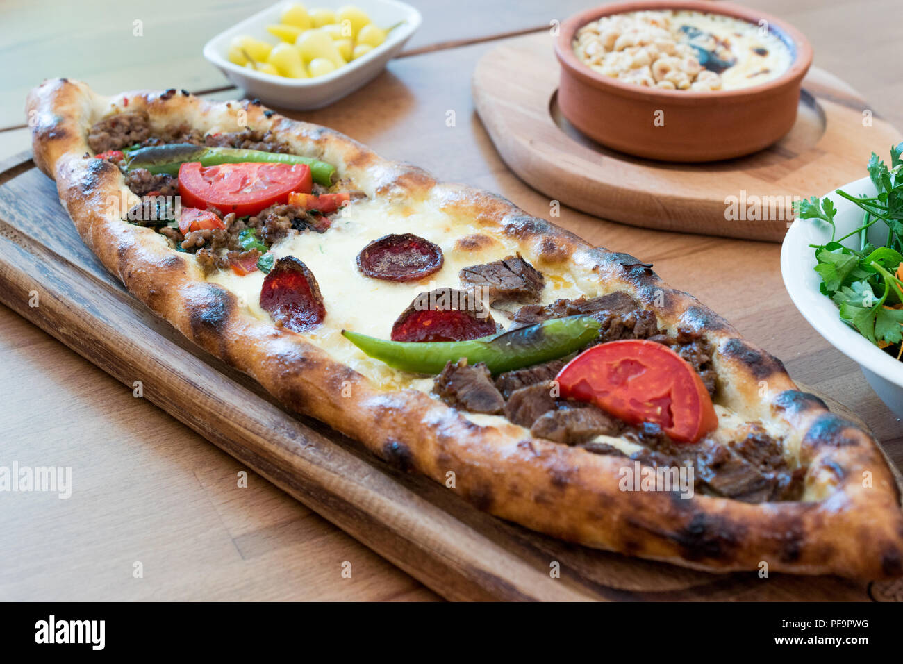 Türkische gemischt Pide mit Hackfleisch, Käse, Wurst (sucuk), Tomaten und Paprika, serviert mit Salat und Gurken. Traditionelle Speisen. Stockfoto