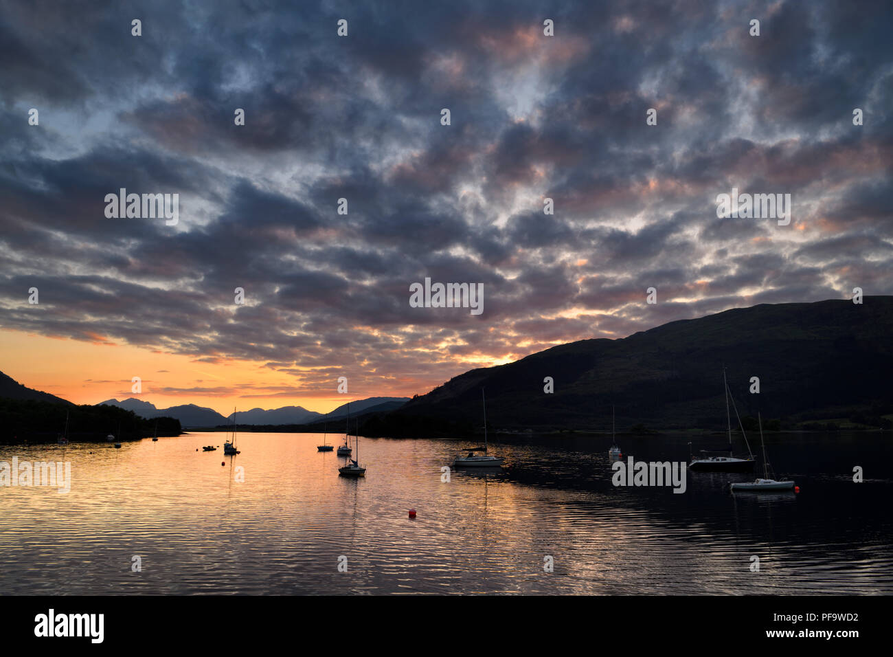 Roter Sonnenuntergang mit Wolken am Loch Leven mit festgebundene Segelboote in Glencoe Yacht Club und die Berge in der Ferne der Schottischen Highlands Schottland Großbritannien Stockfoto