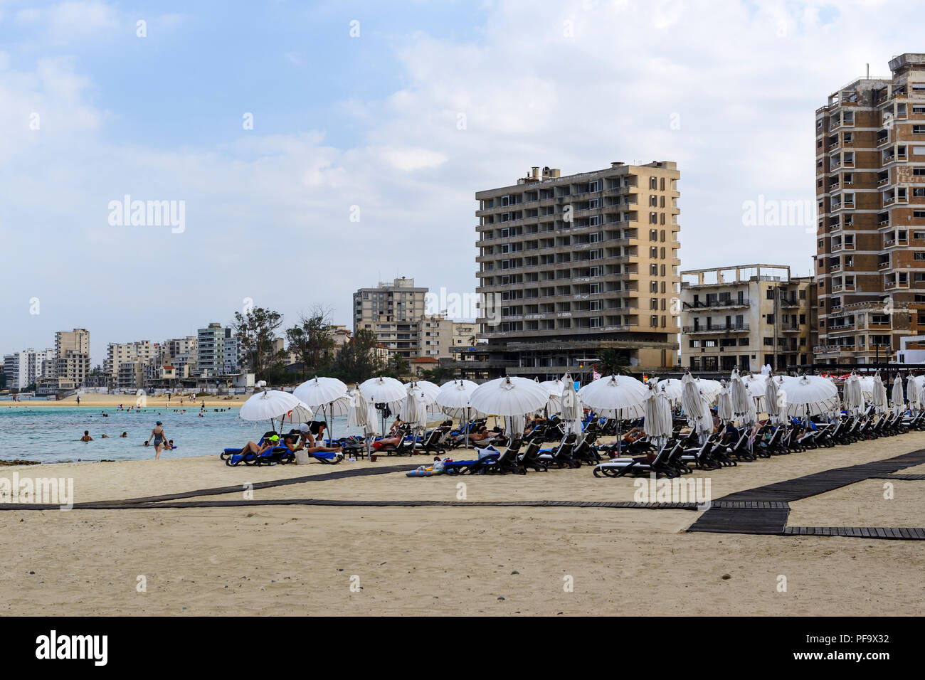 Touristen auf Palm Beach in Famagusta (Gazimagusa) mit verlassenen Hotels und Wohnblocks im Hintergrund, Türkische Republik Nordzypern Stockfoto