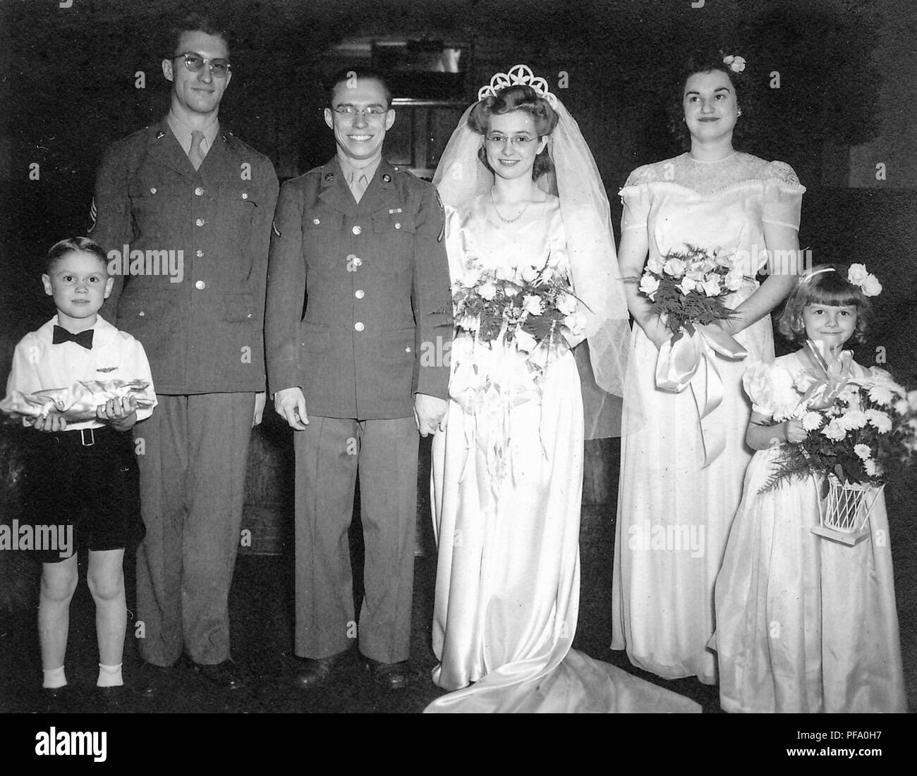 Schwarz-weiß Foto, zeigt ein Bräutigam in eine militärische Uniform und Gläser, neben einem Braut trug ein weißes Kleid, Schleier, Tiara, und Gläser, durch den besten Mann flankiert (auch in Uniform) und eine junge Ring bearer auf der Linken, die Mädchen der Ehre und eine junge BRAUTJUNGFER (beide mit Blumen) auf der rechten Seite, in Ohio, 1945 fotografiert. () Stockfoto