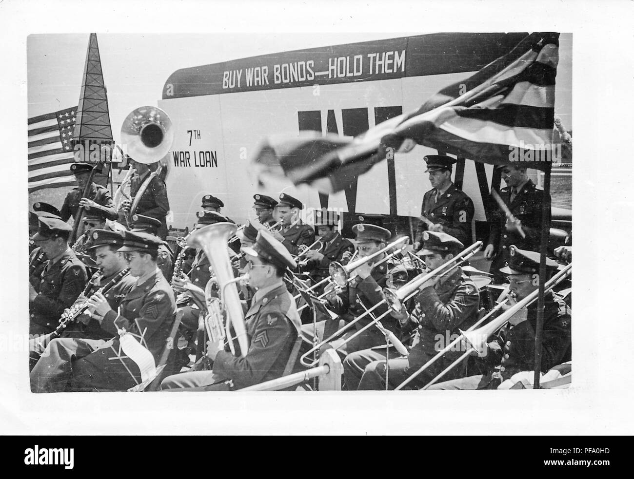 Schwarz-weiß Foto, zeigt eine militärische, Blasmusik, die Musiker tragen militärische Kleidung (mit Flügeln an ihren Ärmel vorschlagen Airforce Zugehörigkeit) und spielen Instrumente außerhalb, mit einem Schild im Hintergrund lesen' kaufen Krieg Anleihen - Sie festhalten," und "7. Krieg Darlehen, "wahrscheinlich in Ohio während des Zweiten Weltkrieges, 1945 fotografiert. () Stockfoto
