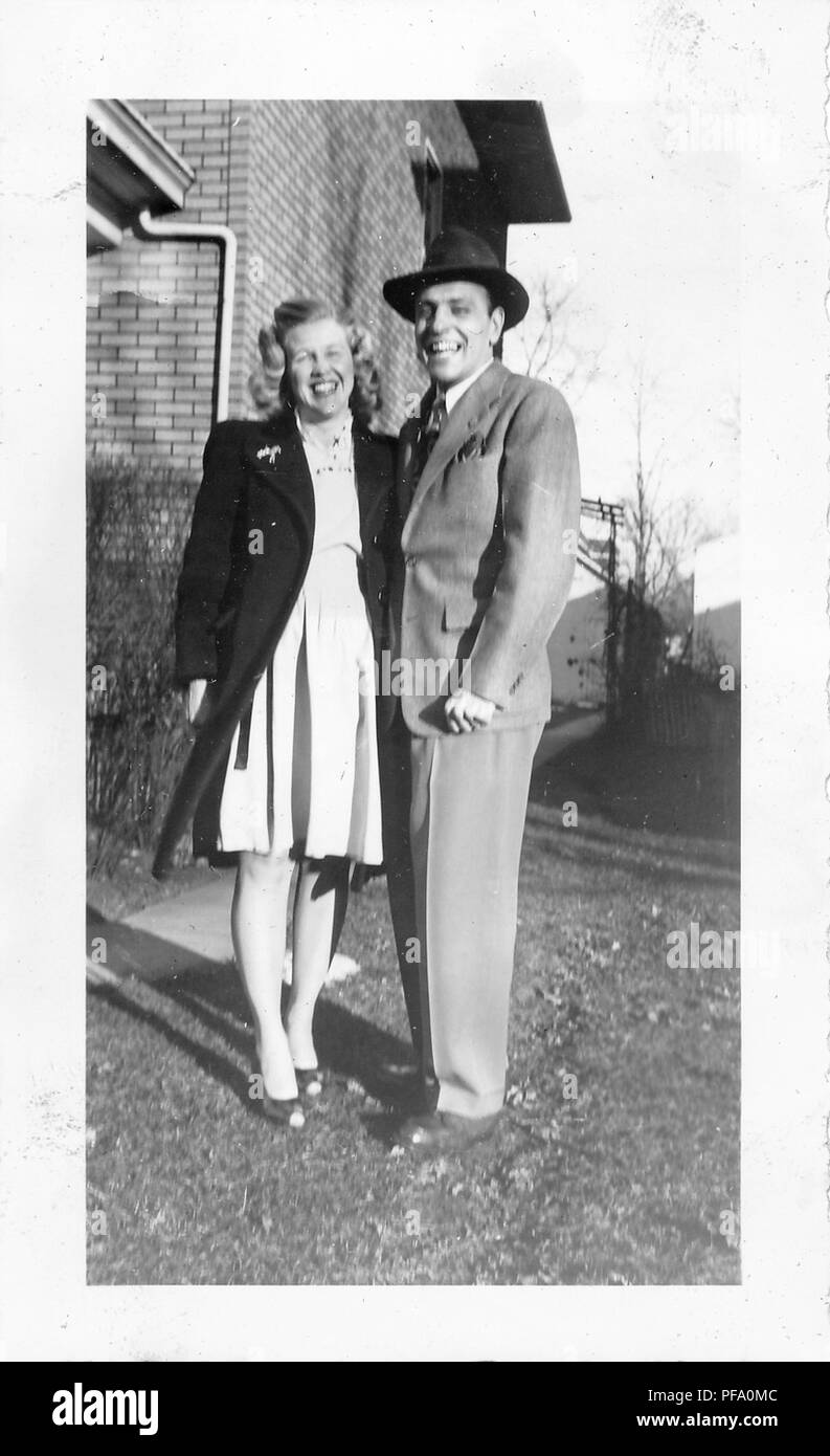 Schwarz-weiß Foto, zeigt ein in voller Länge ansehen Der Mann stand draußen, neben eine blonde Frau, die Frau trägt einen knielangen, helle Kleidung und einer dunklen, knieumspielender Rock mit einer Brosche am Revers, der Mann trägt einen Anzug, Krawatte und Hut, beide vor der Kamera mit einem breiten Lächeln, wahrscheinlich in Ohio in den zehn Jahren fotografierte nach dem Zweiten Weltkrieg, 1955. () Stockfoto