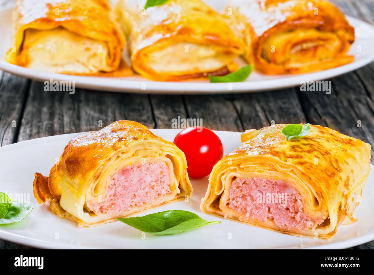Teil der gerollte Pfannkuchen oder Crepes gefüllt mit Hackfleisch und Zwiebeln auf dem ovalen Gerichte mit Cherry Tomaten und Basilikum serviert, Ansicht von oben, in der Nähe - u Stockfoto