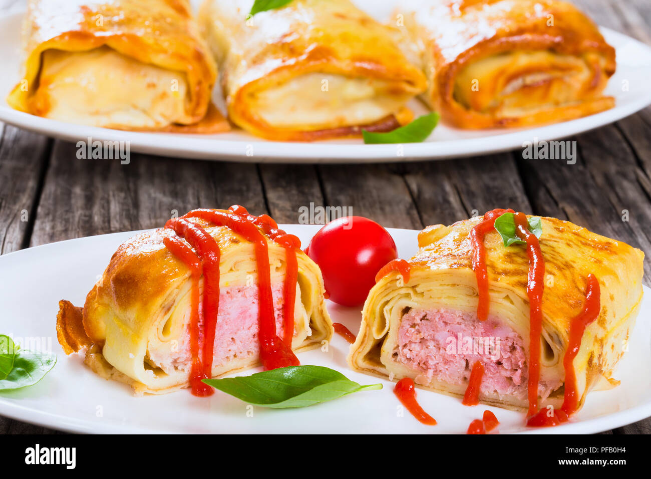 Gerollte Pfannkuchen oder Crepes gefüllt mit Hackfleisch mit Tomatensauce gegossen auf ovalen Gerichte mit Cherry Tomaten und Basilikum serviert, Ansicht von oben, Clo Stockfoto