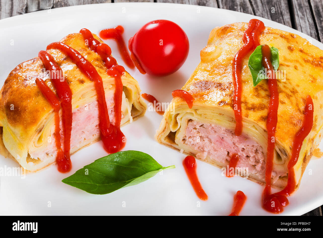 Rolle der Pfannkuchen oder Crepes gefüllt mit Hackfleisch mit Ketchup auf Teller mit Cherry Tomaten und Basilikum serviert gegossen, Ansicht von oben, close-up Stockfoto