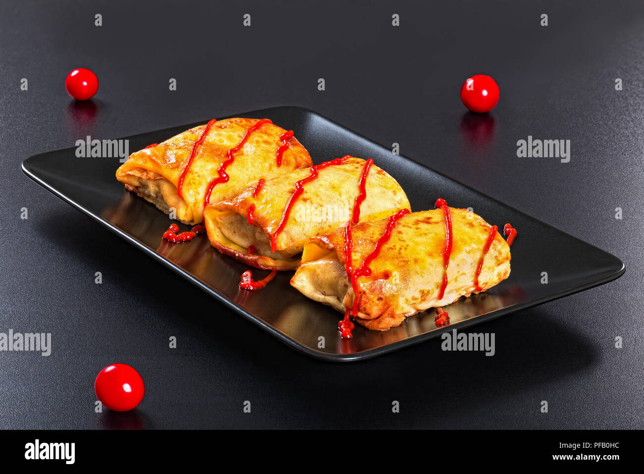 Gerollte Pfannkuchen oder Crepes gefüllt mit Hackfleisch und Gemüse mit Tomatensauce auf schwarzem Teller gegossen, auf dunklem Hintergrund, Ansicht von oben, in der Nähe - u Stockfoto