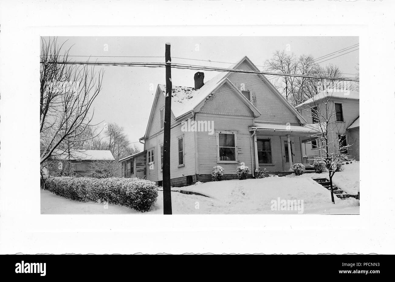 Schwarz-weiß Foto, mit einem kleinen, hellen Haus mit Gleisanschluss, eine überdachte Veranda, und Schnee auf dem Dach sichtbar, Vorgarten, Hecken, blattlosen Bäume und elektrische Beiträge, wahrscheinlich in Ohio in den zehn Jahren fotografierte nach dem Zweiten Weltkrieg, 1950. () Stockfoto