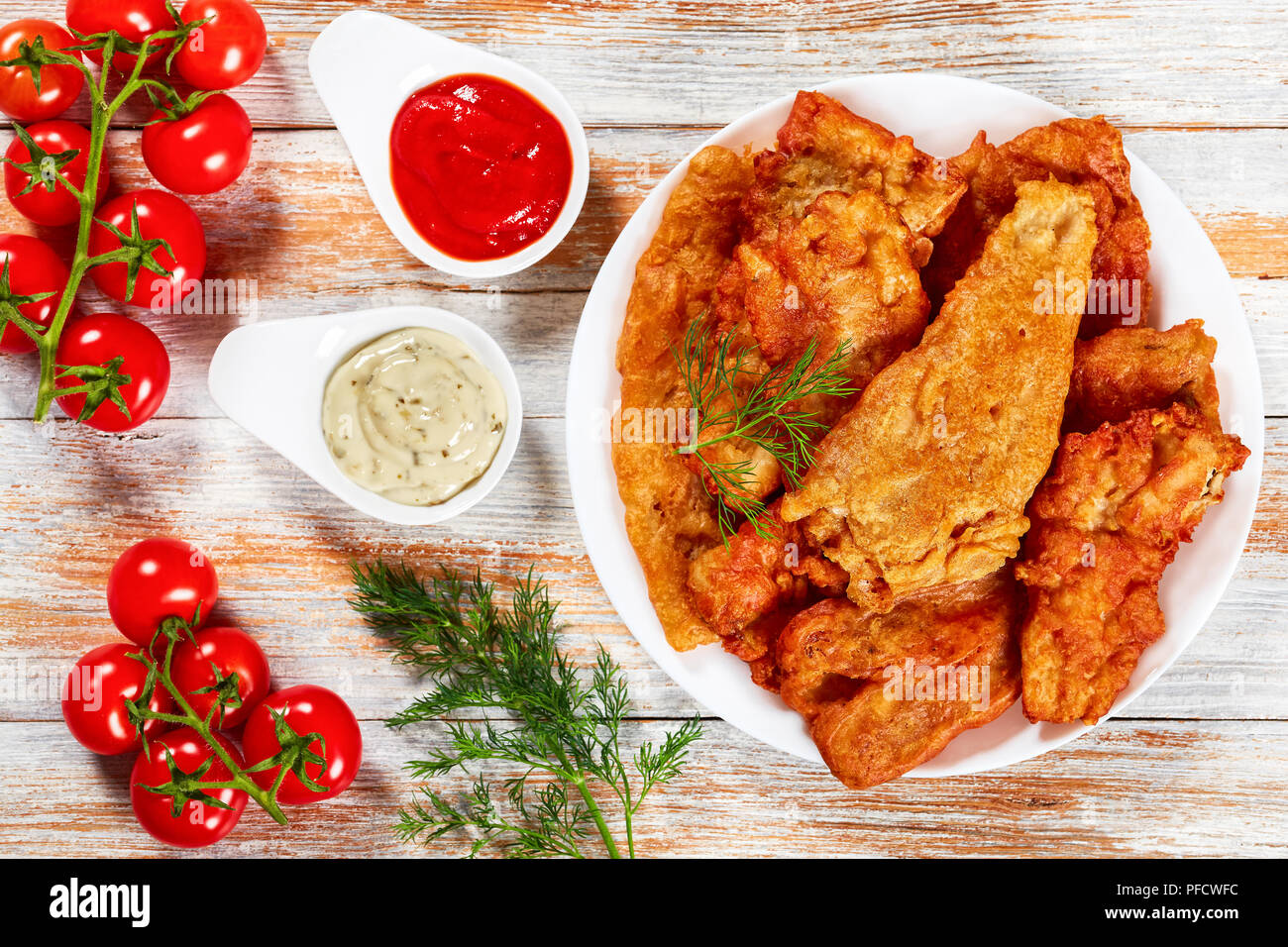 Lecker knusprig gebratene Bier zerschlagene Fischfilets auf weiße Platte auf alten Holztisch. Ketchup und Sauce Tartar in Soße Boote, Dill und Cherry tom Stockfoto