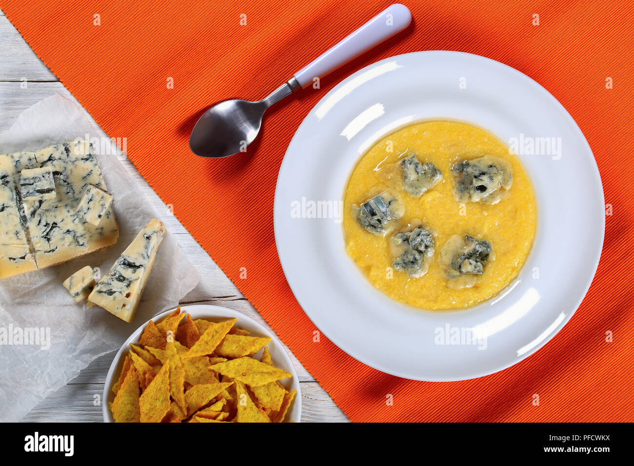 Hot köstlich cremiger Polenta mit geschmolzenen Gorgonzola Käse auf die weiße Platte auf orange table Mat mit Löffel. stück Gorgonzola auf Papier, Kekse in Bo Stockfoto