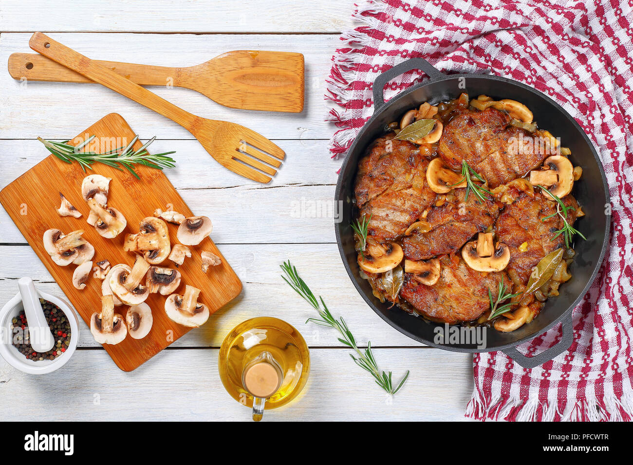 Köstliches Schweinefilet Eintopf mit Zwiebel, Pilze, Rosmarin, halbtrocken Weißwein und Gewürzen in Eisen Eintopf pan am weißen Tisch mit Holzspatel, einfach Stockfoto