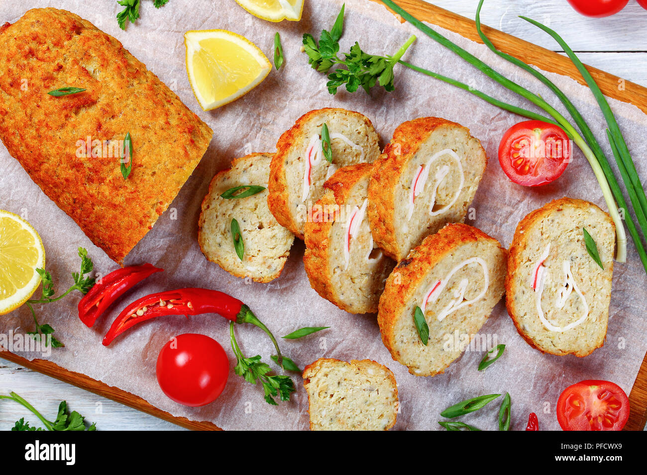In der Nähe von köstlichen Backwaren in den Ofen Gefilte Hackfleisch Weißfischfilet Roll-up in Scheiben geschnitten auf Schneidebrett mit Frühlingszwiebeln, Frischer Frühling Petersilie, Lem Stockfoto