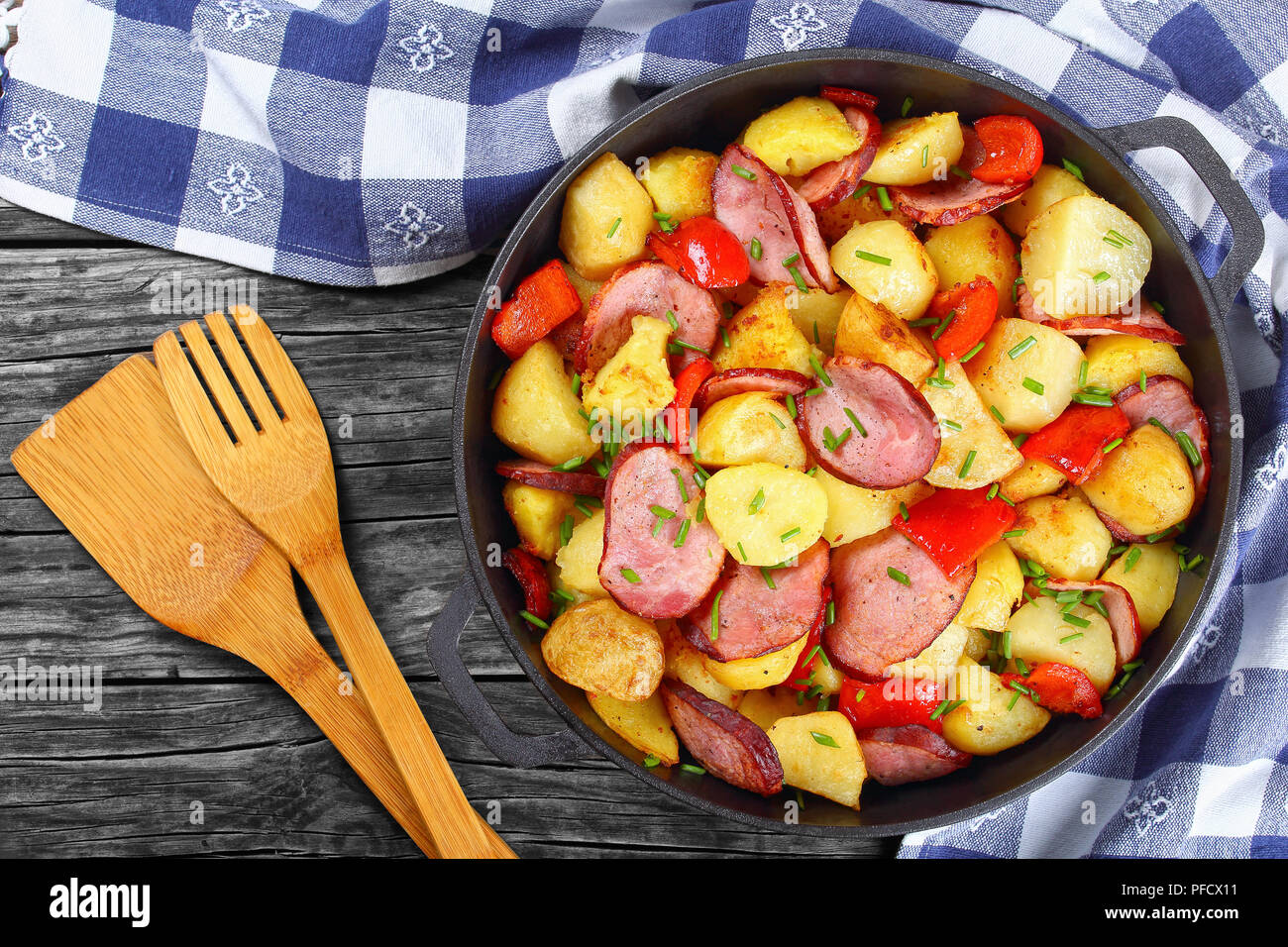 Lecker gebratenen Kartoffelecken mit Schinken und rote Paprika, bestreut mit frischem Grün Frühlingszwiebel in eiserne Pfanne auf dunklen rustikalen Tisch mit Küchentuch, Stockfoto