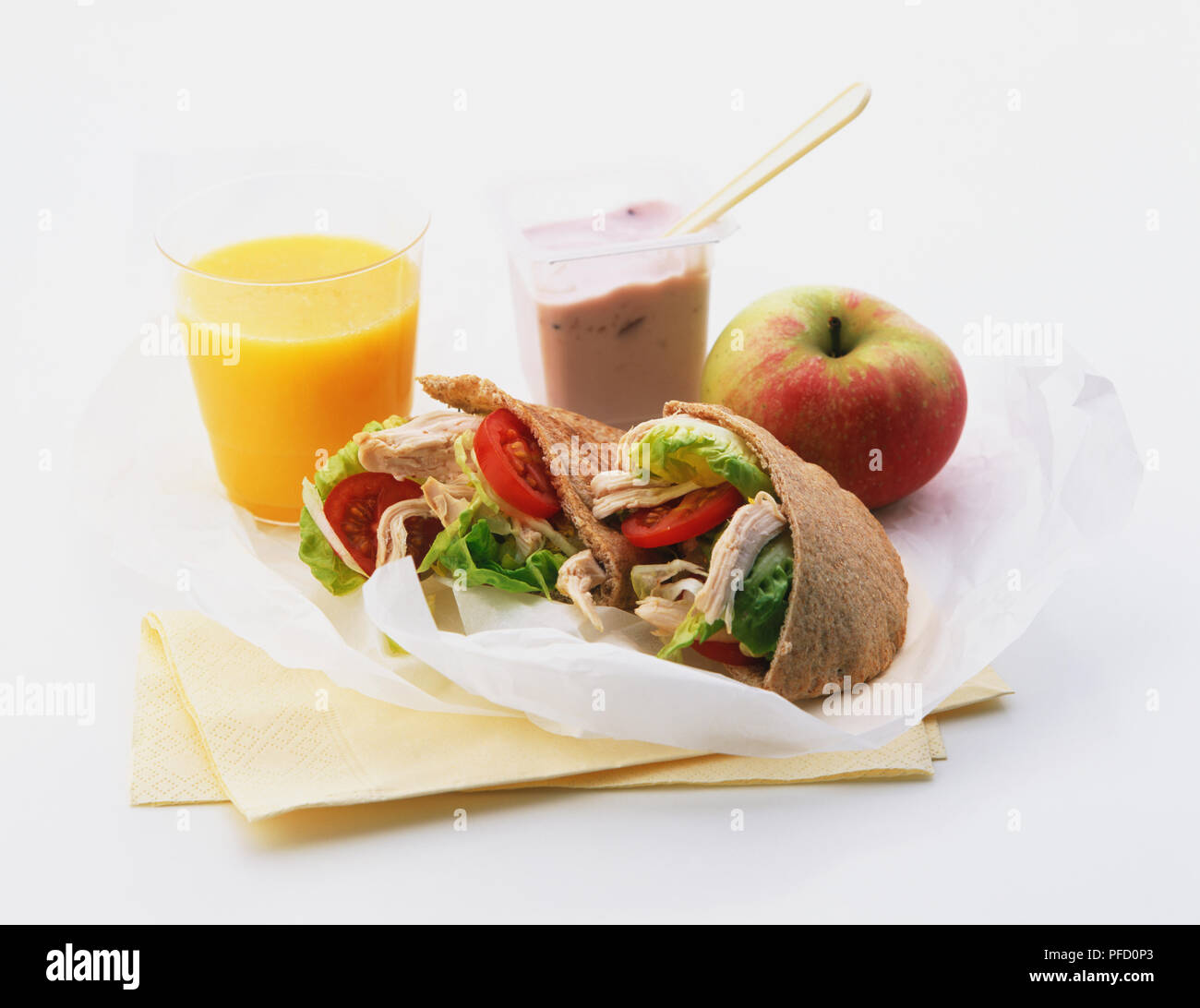 Vollkorn Fladenbrot gefüllt mit Salat und weißes Fleisch, Glas Orangensaft, Obst, Joghurt, Apple. Stockfoto