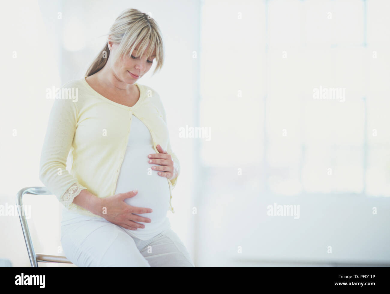 Sitzung blonde Frau im späten Stadium der Schwangerschaft nach unten schauen und streicheln Ihren Bauch, Vorderansicht. Stockfoto