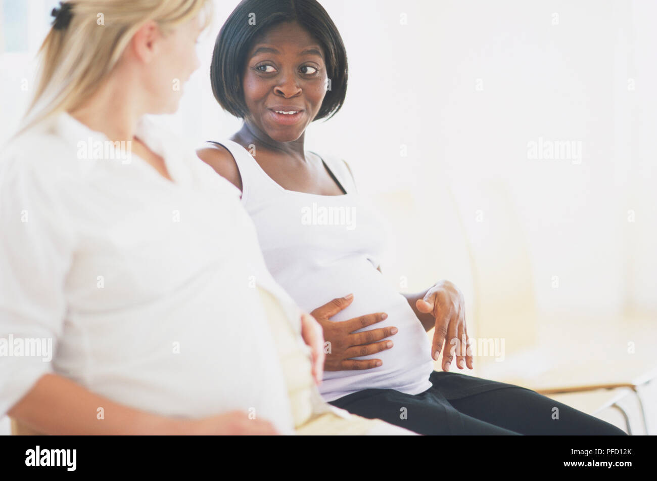 Zwei schwangere Frauen nebeneinander sitzen, streicheln Ihren Bauch und plaudern, Seitenansicht. Stockfoto