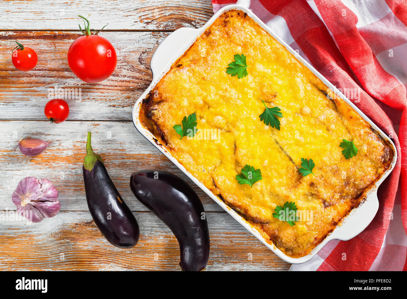 Moussaka, authentische Rezept - Schichten der Aubergine, Hackfleisch, Tomate, béchamelsoße Sauce und Käse in Schale mit küchentuch, frische Auberginen, Knoblauch ein Stockfoto