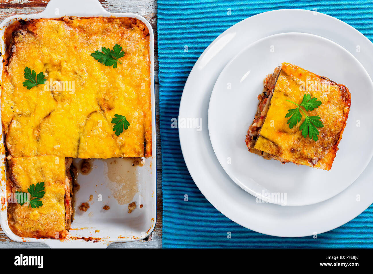Teil der leckeren Moussaka mit Petersilie für authentische Rezept gekocht eingerichtet, auf Platten und in der auflaufform auf Tisch Matte, auf weissem abblätternde Farbe b Stockfoto